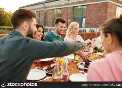 food, leisure and people concept - happy friends eating burgers at dinner party on rooftop in summer. friends eating burgers at dinner party on rooftop