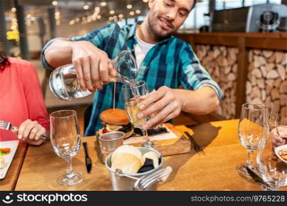 food, leisure and people concept - happy smiling man having dinner at restaurant and pouring water from jug to glass. happy smiling pouring water to glass at restaurant