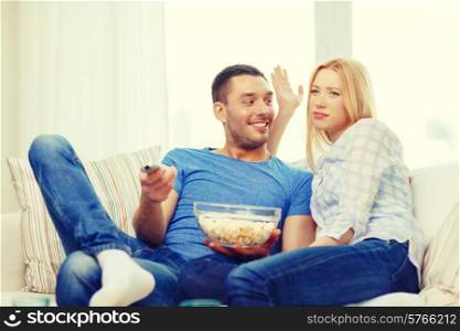food, love, family and happiness concept - smiling couple with popcorn choosing what to watch at home