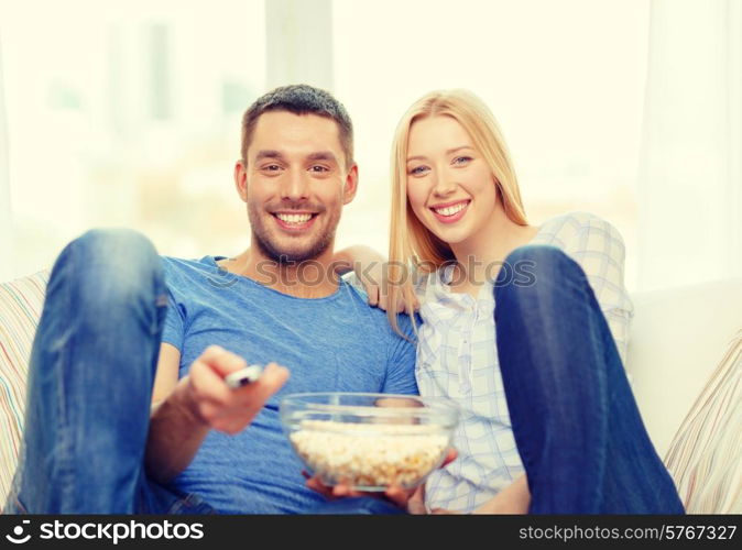 food, love, family and happiness concept - smiling couple with popcorn watching movie at home