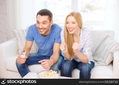 food, love, family, sports, entertainment and happiness concept - smiling couple with popcorn cheering sports team at home