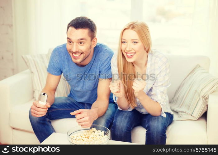 food, love, family, sports, entertainment and happiness concept - smiling couple with popcorn cheering sports team at home