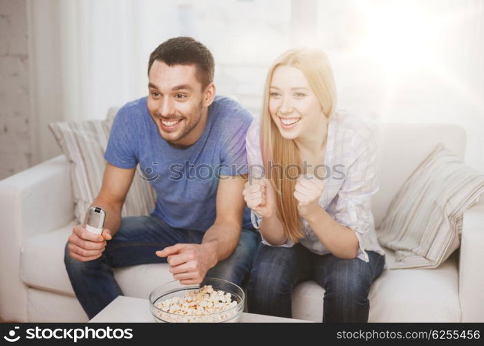 food, love, family, sports, entertainment and happiness concept - smiling couple with popcorn cheering sports team at home