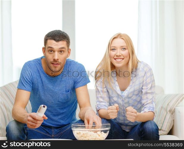 food, love, family, sports, entretainment and happiness concept - smiling couple with popcorn cheering sports team at home