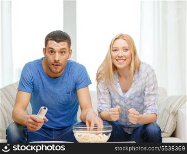 food, love, family, sports, entretainment and happiness concept - smiling couple with popcorn cheering sports team at home