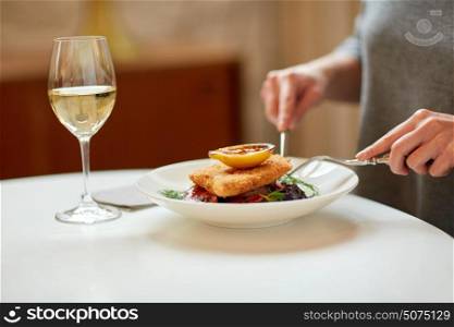 food, new nordic cuisine and people concept - woman eating breaded fish fillet with oven-baked beetroot and tomato salad with fork and knife at cafe or restaurant. woman eating fish salad at cafe or restaurant