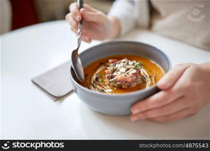 food, new nordic cuisine and people concept - woman eating vegetable pumpkin-ginger cream soup with goat cheese and tomato salad with yogurt in bowl at cafe or restaurant