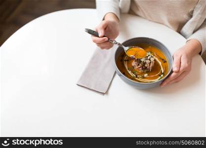 food, new nordic cuisine and people concept - woman eating vegetable pumpkin-ginger cream soup with goat cheese and tomato salad with yogurt in bowl at cafe or restaurant. woman eating pumpkin cream soup at restaurant
