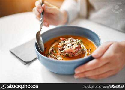food, new nordic cuisine and people concept - woman eating vegetable pumpkin-ginger cream soup with goat cheese and tomato salad with yogurt in bowl at cafe or restaurant. woman eating pumpkin cream soup at restaurant