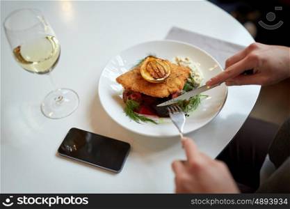 food, new nordic cuisine and people concept - woman with smartphone eating breaded fish fillet with tartar sauce and oven-baked beetroot tomato salad with fork and knife at cafe or restaurant