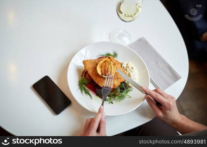 food, new nordic cuisine and people concept - woman with smartphone eating breaded fish fillet with tartar sauce and oven-baked beetroot tomato salad with fork and knife at cafe or restaurant