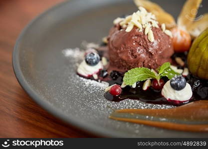 food, new nordic cuisine and sweets concept - close up of chocolate ice cream dessert with blueberry kissel, honey baked fig and greek yoghurt on plate at restaurant