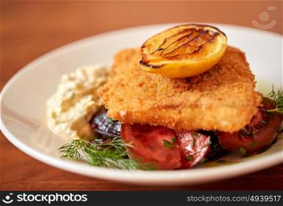 food, new nordic cuisine, culinary and cooking concept - close up of breaded fish fillet with tartar sauce and oven-baked beetroot tomato salad on plate. close up of fish salad with roasted lemon on plate