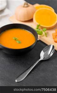 food, new nordic cuisine, culinary and cooking concept - close up of vegetable pumpkin cream soup in bowl and spoon on stone table. close up of vegetable pumpkin cream soup in bowl