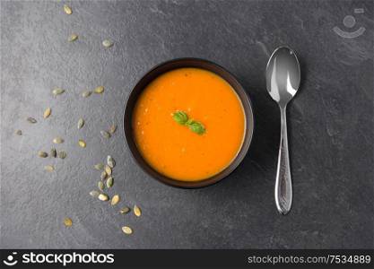 food, new nordic cuisine, culinary and cooking concept - close up of vegetable cream soup in bowl, pumpkin seeds and spoon on slate stone background. vegetable pumpkin cream soup in bowl with spoon