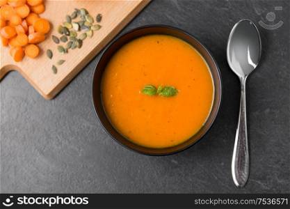 food, new nordic cuisine, culinary and cooking concept - close up of pumpkin cream soup in bowl, spoon and cutting board with vegetables on slate stone background. vegetable pumpkin cream soup in bowl with spoon