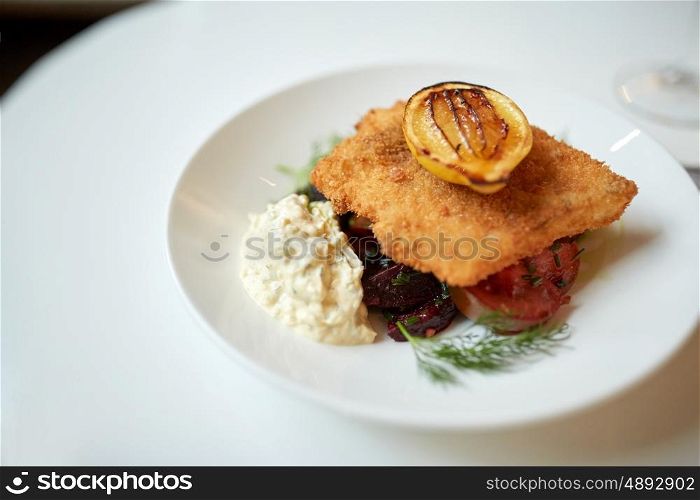 food, new nordic cuisine, dinner, culinary and cooking concept - close up of breaded fish fillet with tartar sauce and oven-baked beetroot tomato salad on plate