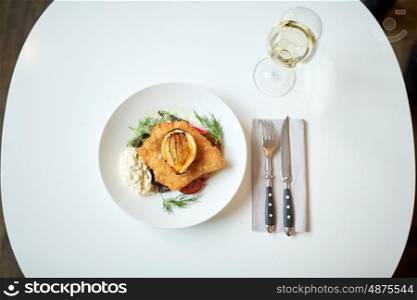 food, new nordic cuisine, dinner, culinary and cooking concept - fish salad with breaded fish fillet with tartar sauce and oven-baked beetroot tomato salad and glass of white wine on restaurant table