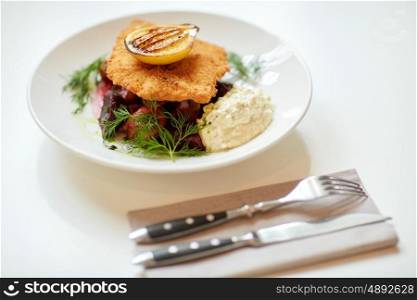 food, new nordic cuisine, dinner, culinary, haute cuisine and cooking concept - close up of breaded fish fillet with tartar sauce and oven-baked beetroot tomato salad on plate