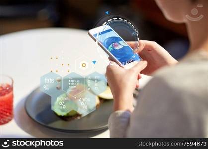 food, new nordic cuisine, technology and people concept - close up of woman with toast skagen on smartphone screen and nutritional value chart at restaurant. hands with phone and food nutritional value chart