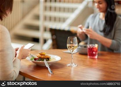 food, new nordic cuisine, technology and people concept - women with smartphones having breaded fish fillet with tartar sauce and oven-baked beetroot tomato salad for dinner at restaurant