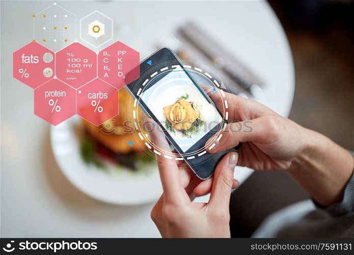 food, new nordic cuisine, technology, eating and people concept - close up of hands with breaded fish fillet on smartphone screen and nutritional value chart at restaurant. hands with phone and food nutritional value chart