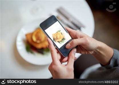 food, new nordic cuisine, technology, eating and people concept - woman with smartphone photographing breaded fish fillet with tartar sauce and oven-baked beetroot tomato salad at restaurant