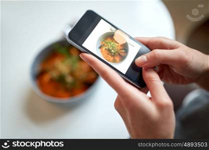 food, new nordic cuisine, technology, eating and people concept - woman with smartphone photographing bowl of seafood soup with fish and blue mussels at restaurant