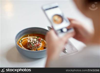 food, new nordic cuisine, technology, eating and people concept - woman with smartphone photographing bowl of vegetable pumpkin-ginger soup with goat cheese and tomato salad with yogurt at restaurant. woman with smartphone photographing food at cafe