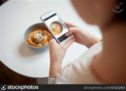 food, new nordic cuisine, technology, eating and people concept - woman with smartphone photographing bowl of vegetable pumpkin-ginger soup with goat cheese and tomato salad with yogurt at restaurant. woman with smartphone photographing food at cafe
