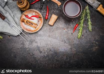 Food or cooking background with herbs , spices , meat fork and knife and glass of red wine on dark rustic metal background, top view, border