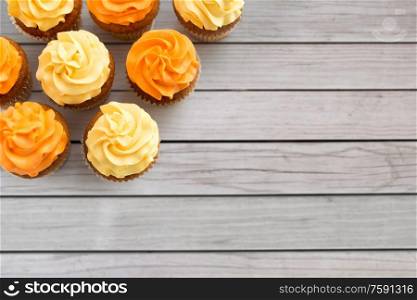 food, pastry and confectionery concept - cupcakes with buttercream frosting over grey wooden boards background. cupcakes with frosting on wooden boards background