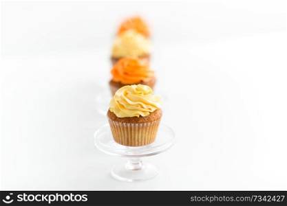 food, pastry and sweets concept - cupcakes with buttercream frosting on glass confectionery stand over white background. cupcakes with frosting on confectionery stands