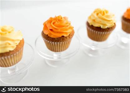food, pastry and sweets concept - cupcakes with buttercream frosting on glass confectionery stand over white background. cupcakes with frosting on confectionery stands