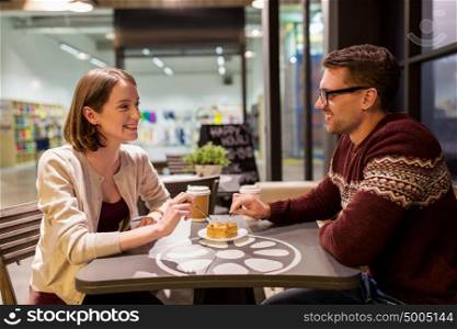 food, people and dating concept - happy couple eating peace of cake or pie for dessert at cafe. happy couple eating cake for dessert at cafe