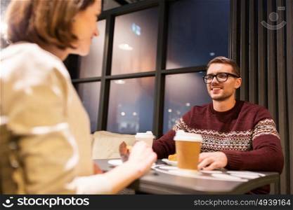food, people and dating concept - happy couple with coffee in paper cups eating cake or pie for dessert at cafe. happy couple with coffee eating cake at cafe