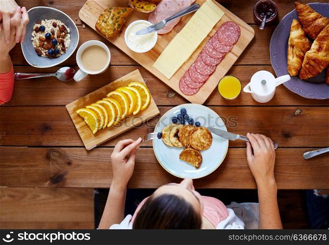 food, people and family concept - woman with fork and knife eating pancakes for breakfast at wooden table. woman with food on table eating pancakes