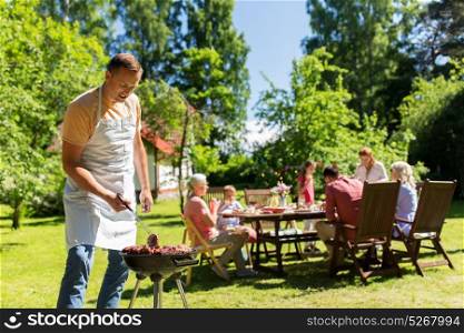 food, people and family time concept - man cooking meat on barbecue grill at summer garden party. man cooking meat on barbecue grill at summer party