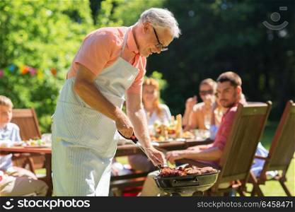 food, people and family time concept - senior man cooking meat on barbecue grill at summer garden bbq party. senior man cooking meat on barbecue grill outdoors