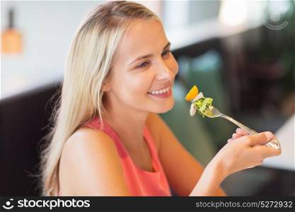 food, people and leisure concept - happy young woman eating salad for lunch at restaurant. happy young woman eating at restaurant