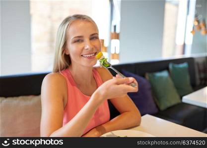 food, people and leisure concept - happy young woman eating salad for lunch at restaurant. happy young woman eating at restaurant