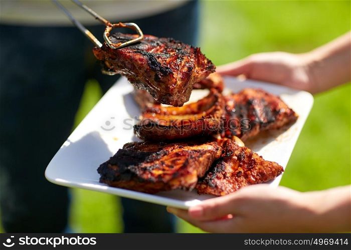 food, people, eating and cooking concept - man with tongs putting barbecue meat on plate at summer party. man cooking meat at summer party barbecue