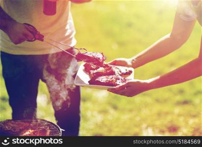 food, people, eating and cooking concept - man with tongs putting barbecue meat on plate at summer party. man cooking meat at summer party barbecue