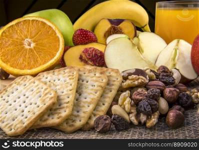 Food photography with a delicious and nutritious meal, formed of fresh fruits, a mix of nuts, salty crackers and a glass of orange juice.