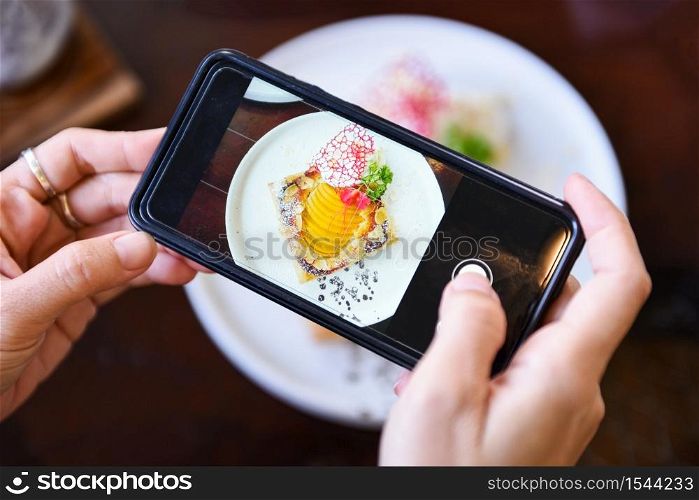 Food photography woman hands make photo cake with smartphone / taking photo food for post and share on social networks with camera smart phone in restaurant