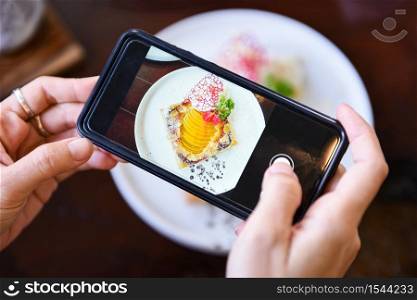 Food photography woman hands make photo cake with smartphone / taking photo food for post and share on social networks with camera smart phone in restaurant