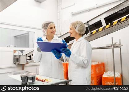 food production, industry and people concept - happy women technologists with clipboard tasting ice cream quality at factory. women technologists tasting ice cream at factory