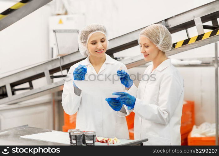 food production, industry and people concept - happy women technologists with clipboard tasting ice cream quality at factory. women technologists tasting ice cream at factory