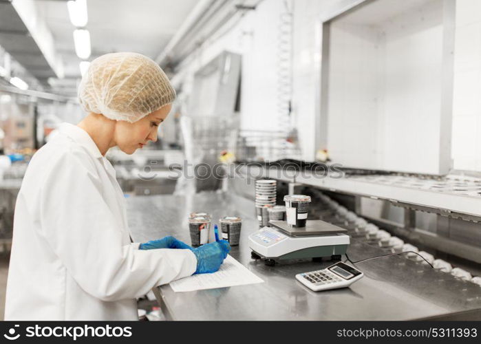 food production, industry and people concept - woman weighing ice cream on scale and filling papers at factory. woman working at ice cream factory