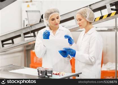 food production, industry and people concept - women technologists with clipboard tasting ice cream quality at factory. women technologists tasting ice cream at factory